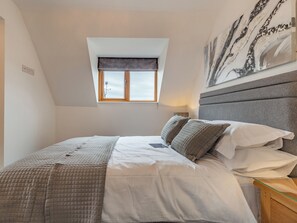A bedroom with a sloped ceiling, a window with a view, a bed with a quilted blanket, and a painting on the wall. - 4 bedroom accommodation in Church Broughton, near Derby (Church Broughton, near Derby)