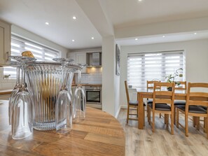 A modern kitchen with a wooden dining table, clear glassware, and wooden chairs. - 4 bedroom accommodation in Church Broughton, near Derby (Church Broughton, near Derby)