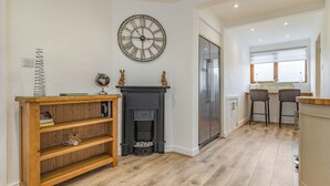 A modern kitchen with a black fireplace, a large wall clock, and a bar area with two stools. - 4 bedroom accommodation in Church Broughton, near Derby (Church Broughton, near Derby)