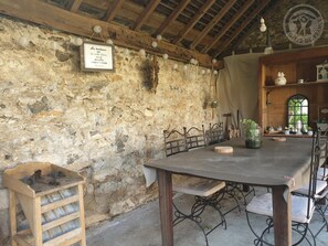 Un mur de pierres apparentes, avec une table et des chaises en bois, un banc en bois et un panneau indicateur.