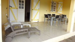 Ein gelbes Gebäude mit einer Terrasse, die einen Tisch und Stühle bietet, einer weißen Tür mit gelbem Akzent und einem gefliesten Boden.