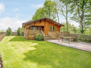 A wooden cabin with a porch, a small garden, and a picnic table.