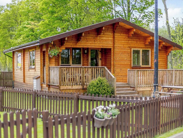 A wooden cabin with a porch, windows, and a fenced yard.