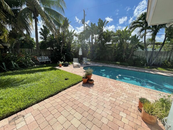 A backyard with a swimming pool, a brick patio, and a wooden fence.