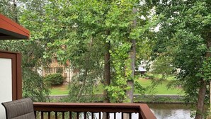 A balcony with a chair overlooking a pond and trees. - Edelweiss River Haus on the river and close to everything in Helen (Helen)