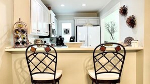 A kitchen with white cabinets, a refrigerator, a coffee maker, and two bar stools with a unique back design. - Edelweiss River Haus on the river and close to everything in Helen (Helen)