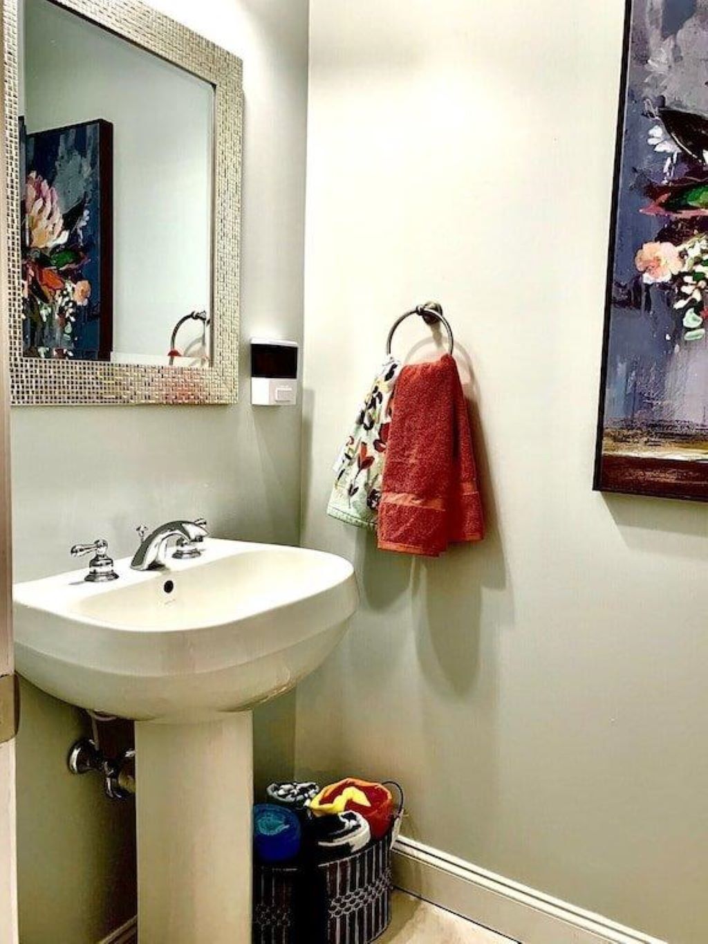 A bathroom with a white sink, a mirror, a towel rack with a red towel, and a trash can.