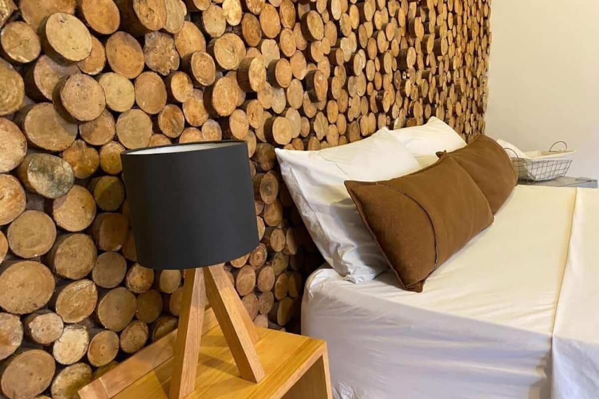 A bedroom with a bed, pillows, a bedside table with a lamp, and a wall covered with stacked logs.