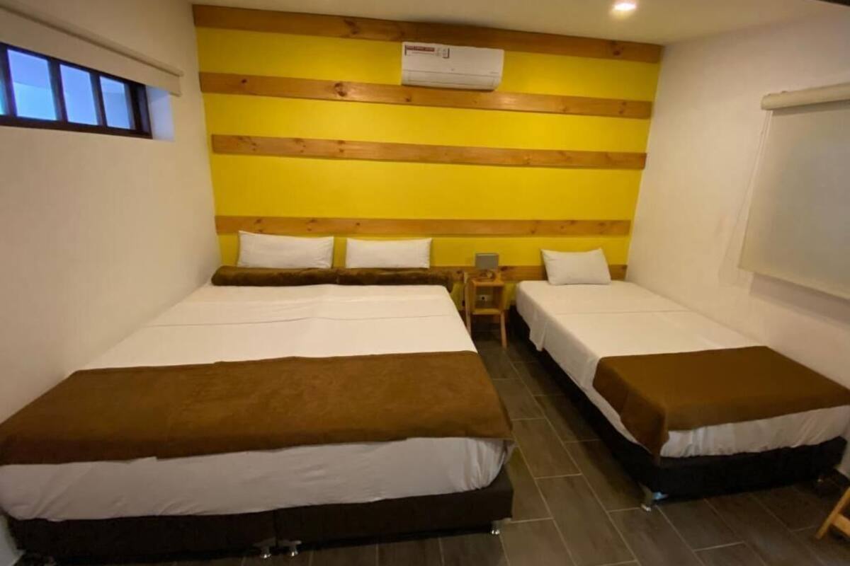 A hotel room with two beds, a wooden headboard, a small bedside table, and a window.