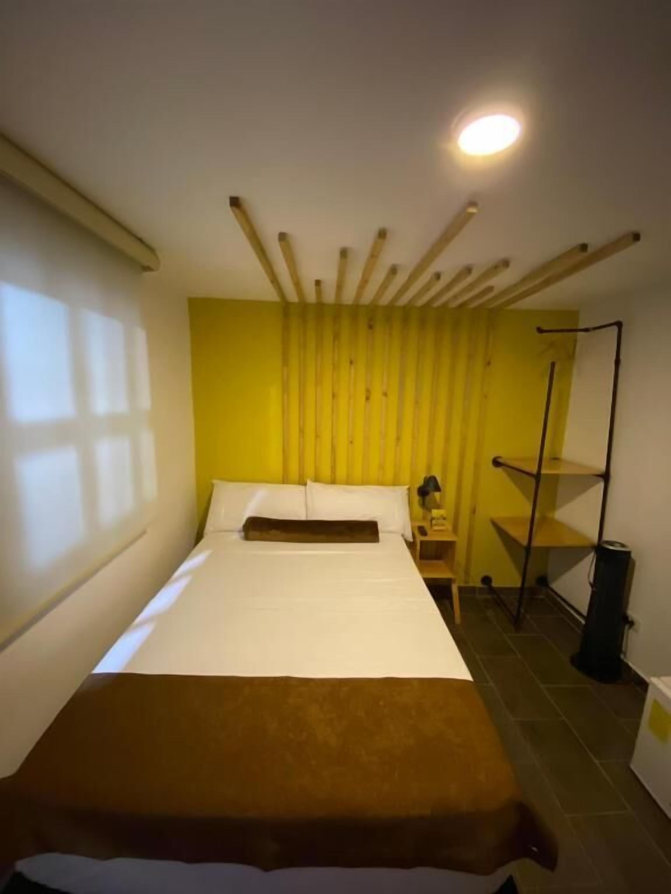 A room with a bed, a bedside table, a lamp, and a shelf unit.