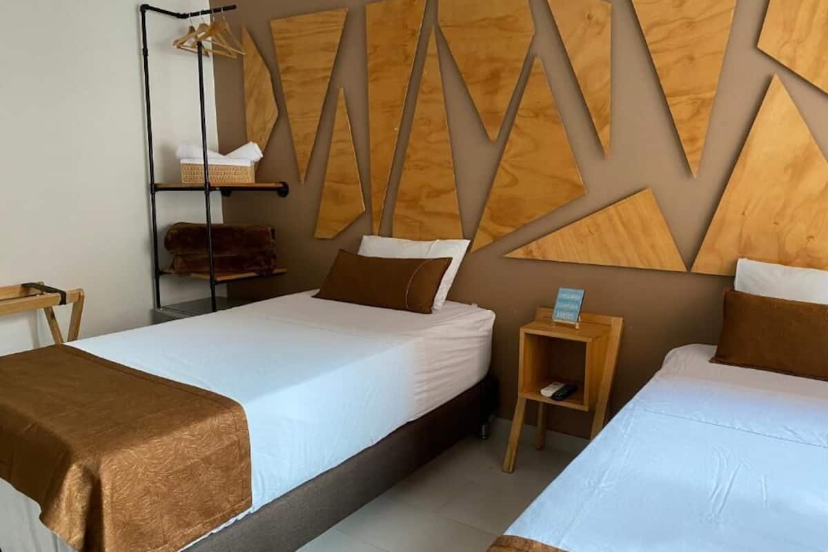 A hotel room with two beds, a wooden shelf unit, and a wall with geometric wooden panels.
