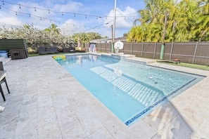 A swimming pool with a tiled deck, a basketball hoop, and a fence.