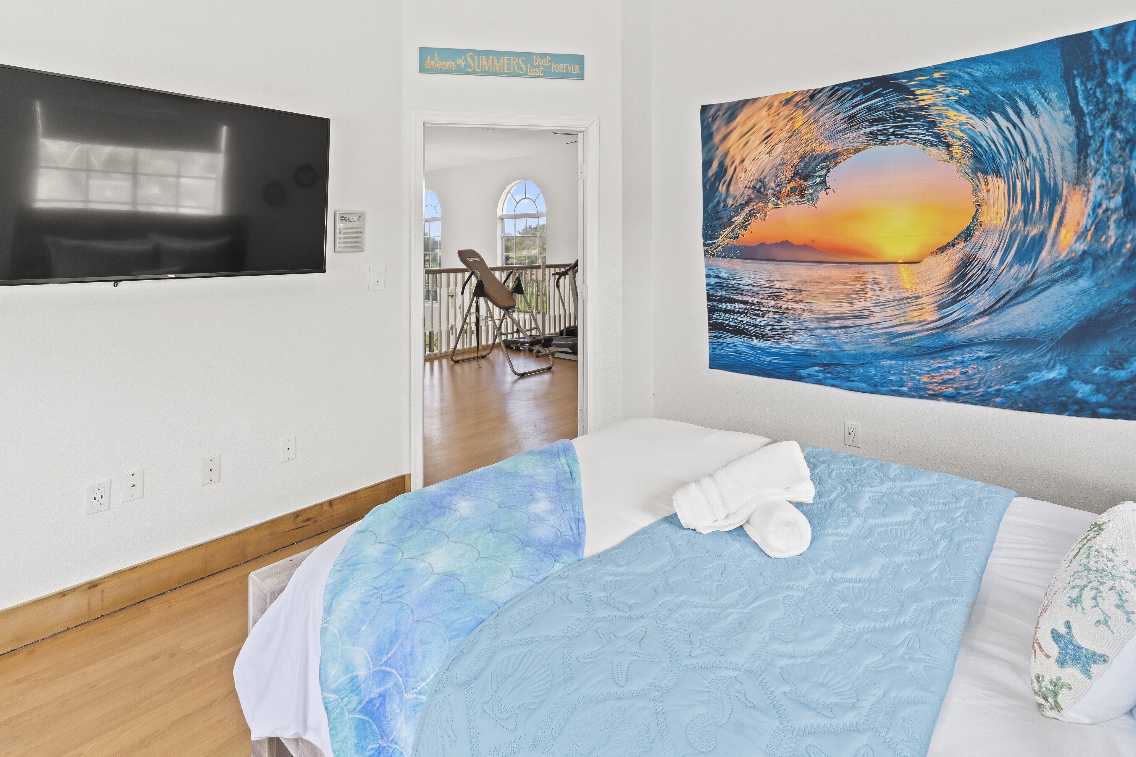 Une chambre à coucher avec un lit, une télévision et un grand tableau représentant une vague.