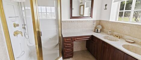 A bathroom with a walk-in shower, a large mirror, a vanity with two sinks, and a window providing a view of the outdoors.
