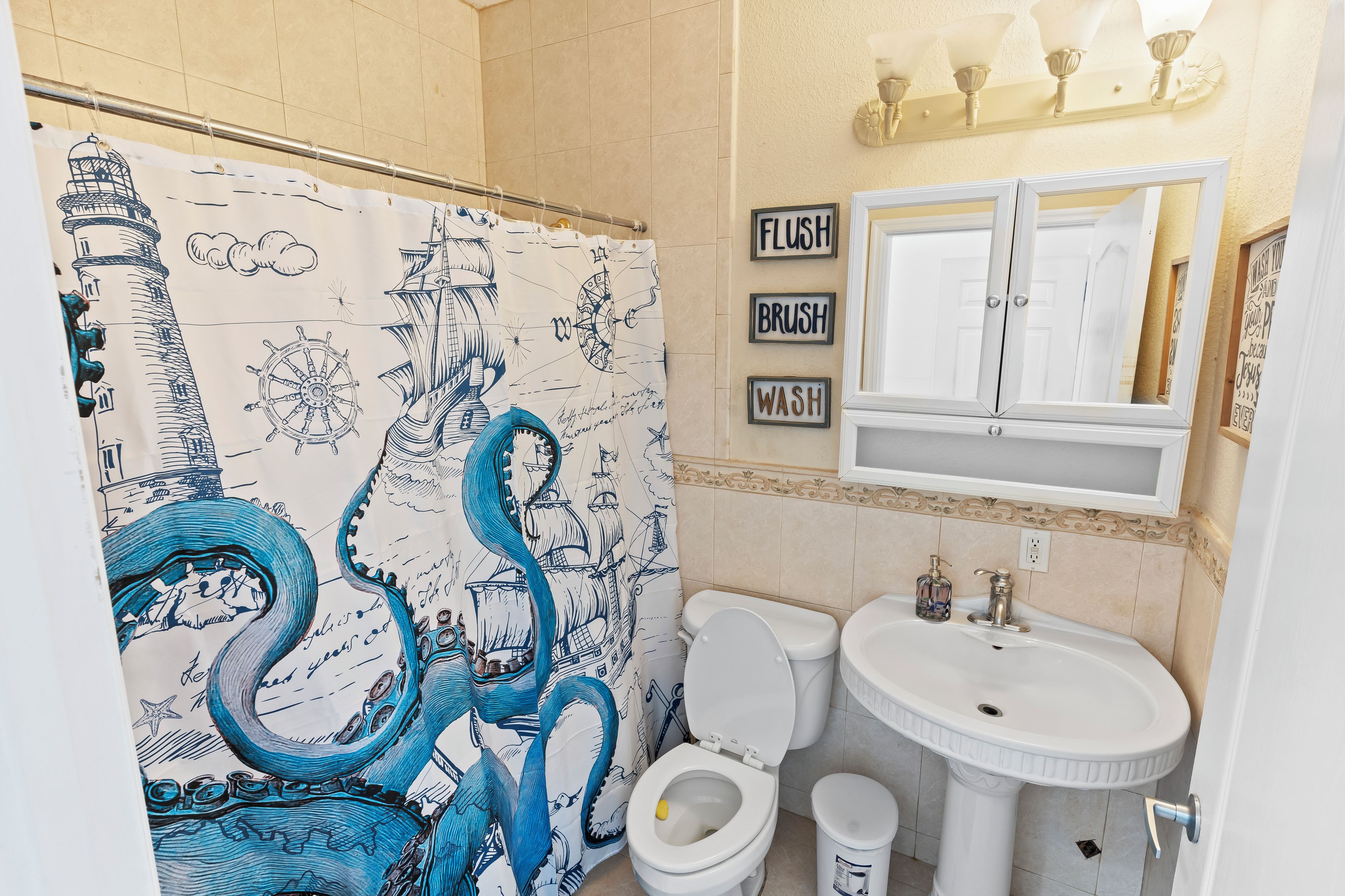 Une salle de bain avec un rideau de douche à motifs nautiques, des toilettes, un lavabo et un miroir au-dessus.
