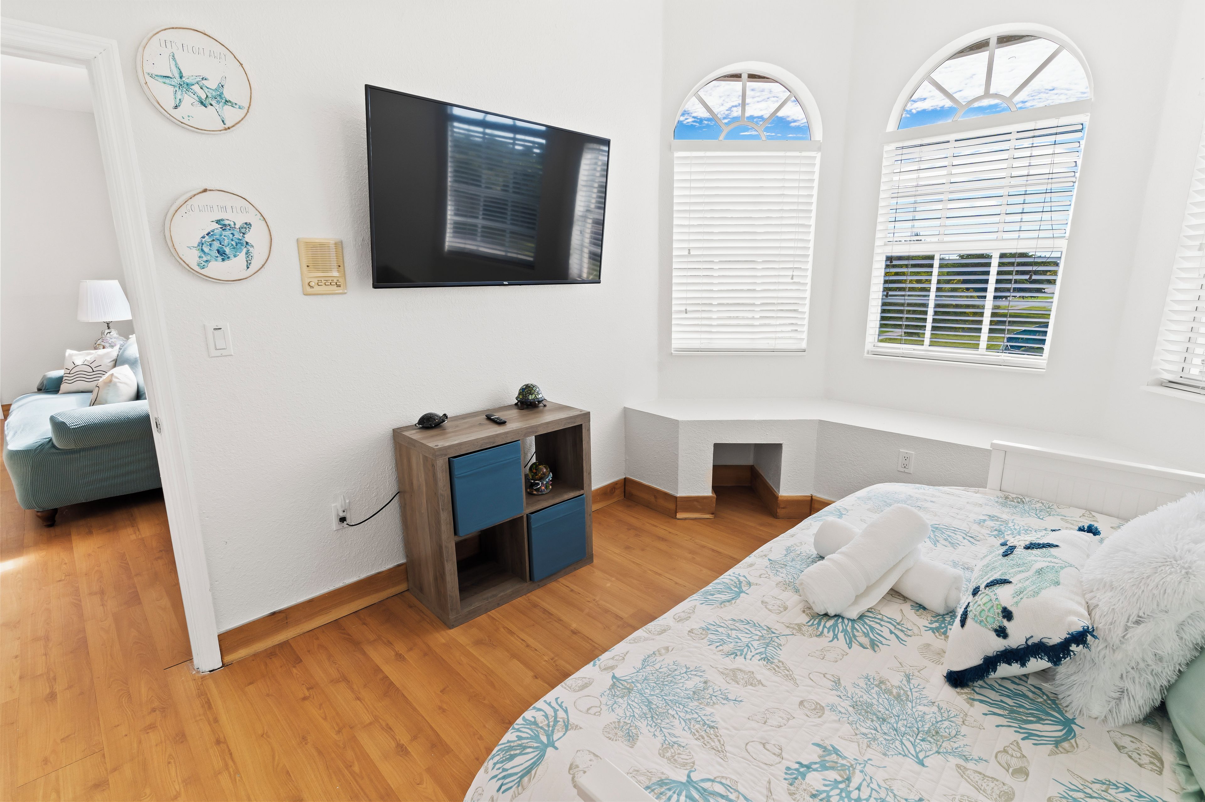 Un dormitorio con cama, televisor, escritorio pequeño y ventana con persianas.