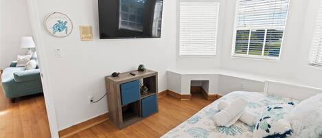 Un dormitorio con cama, televisor, escritorio pequeño y ventana con persianas.