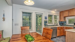A modern kitchen with wooden cabinets, a dining table with chairs, and a built-in dishwasher. - Tranquil Family Home located in Surfman's Walk; private crofter with shoals access (Bald Head Island)