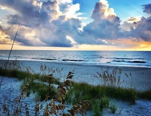 A beach with waves, grassy dunes, and a cloudy sky. - Tranquil Family Home located in Surfman's Walk; private crofter with shoals access (Bald Head Island)