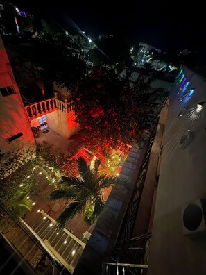 A nighttime view of a courtyard with a red-lit staircase, a palm tree, and surrounding buildings.