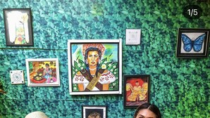 Two people sitting on a wicker bench with a green leafy wall behind them, featuring various framed artworks.