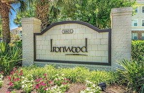 A sign with the name 'Ironwood' and the number '5801' on a brick wall, surrounded by greenery and a palm tree.
