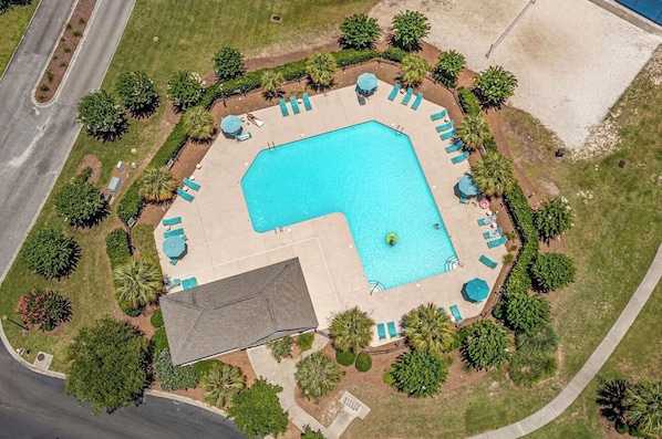 An aerial view of a residential property with a swimming pool, surrounded by a landscaped garden and a paved deck area.