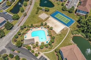 An aerial view of a residential area with a swimming pool, tennis court, and a small pond.