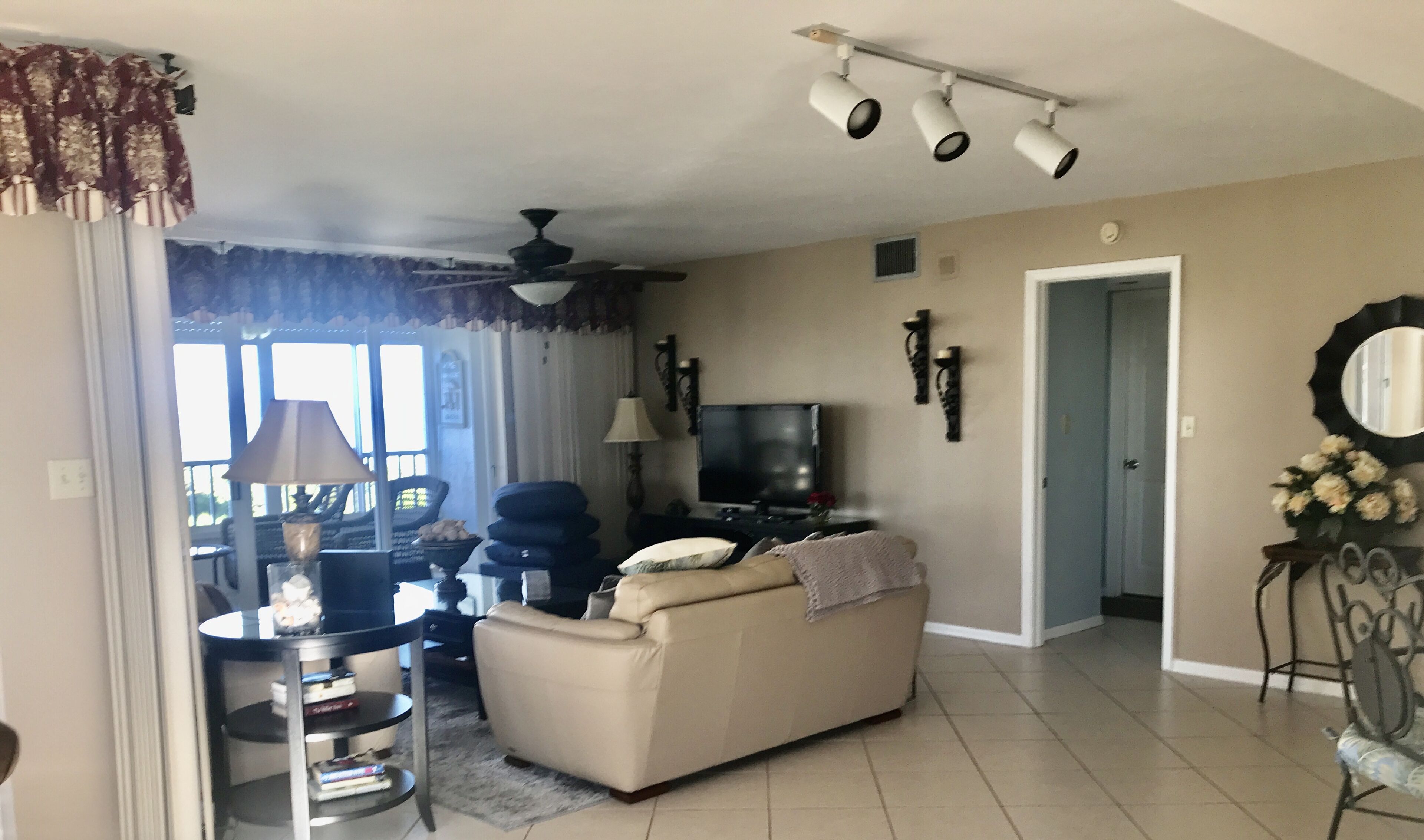 A living room with a sofa, a TV, a ceiling fan, and a dining area with a table and chairs.