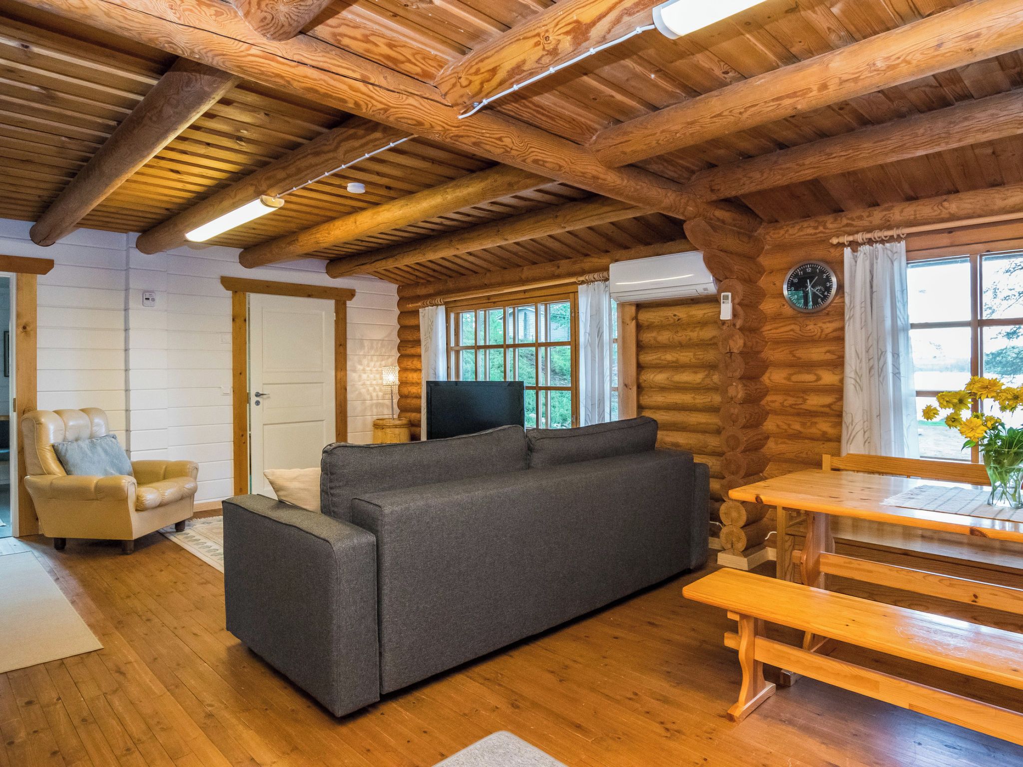 A log cabin interior with a sofa, a wooden table, and a television.