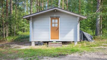 A small, single-story cabin with a wooden door and a small porch, surrounded by a forested area.