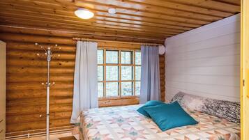 Un dormitorio de cabaña de madera con cama, cortinas, una ventana y una lámpara.