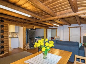 Un salon chaleureux avec un plafond en bois, une cheminée, un canapé et une table à manger agrémentée d’un vase de fleurs.