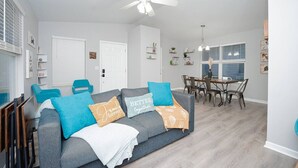 A modern living room with a grey sofa, teal and orange cushions, a white ceiling fan, and a dining area with a wooden table and chairs. - 3bd, 2bth, 1K&2Q, Walk to park! Park 1 car in Ga.! (St. Louis)