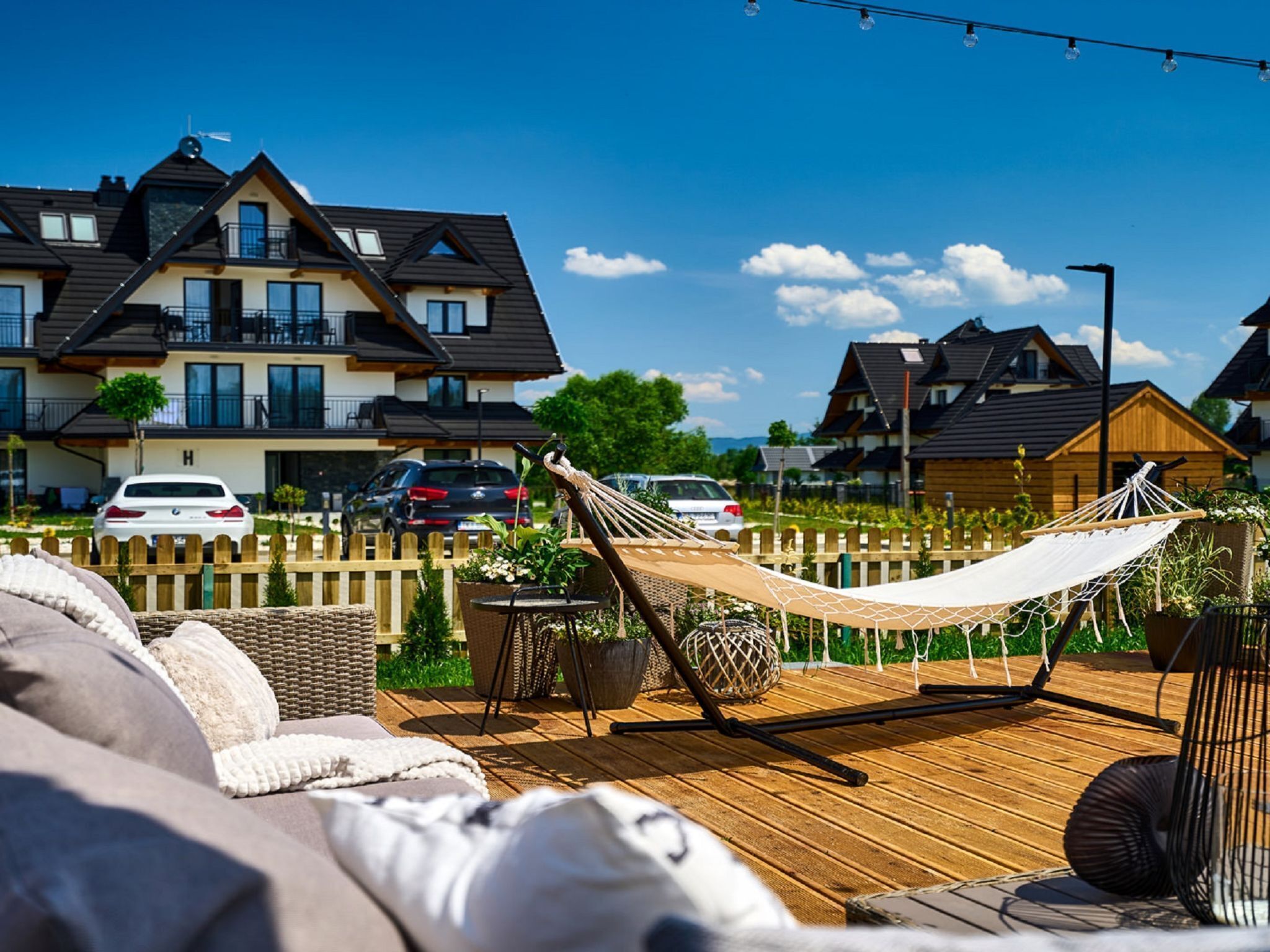 Eine Holzterrasse mit einer Hängematte, Gartenmöbeln und Blick auf Wohnhäuser im Hintergrund.