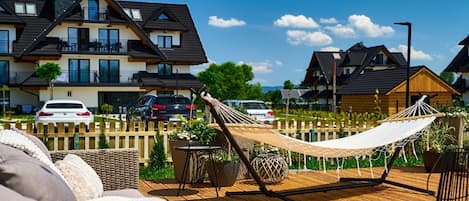 A wooden deck with a hammock, outdoor furniture, and a view of residential buildings in the background.