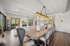 A spacious dining area with a wooden table, upholstered chairs, and a hanging light fixture. - Maynard Rocks IV at Elk Creek - Hot tub, creekside setting, firepit (Banner Elk)