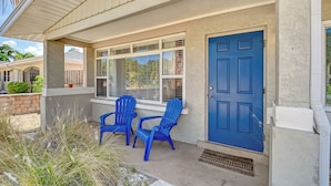 Une maison avec une porte bleue, deux chaises Adirondack bleues et un porche couvert.