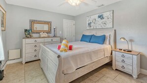Une chambre à coucher comprenant un lit, une table de chevet, une commode, un ventilateur de plafond et des œuvres d’art.