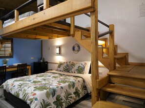 Uma cama beliche com escada de madeira, uma escrivaninha com cadeira e uma cama com colcha estampada.