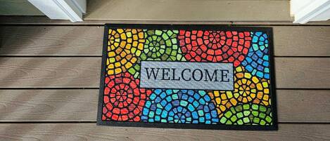 A colorful mosaic welcome mat on a wooden porch.