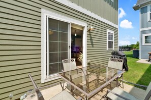 A patio with a glass table and chairs, a sliding glass door, and a small outdoor kitchen area.