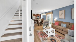 Una sala de estar moderna con una escalera, un comedor y una cocina al fondo.