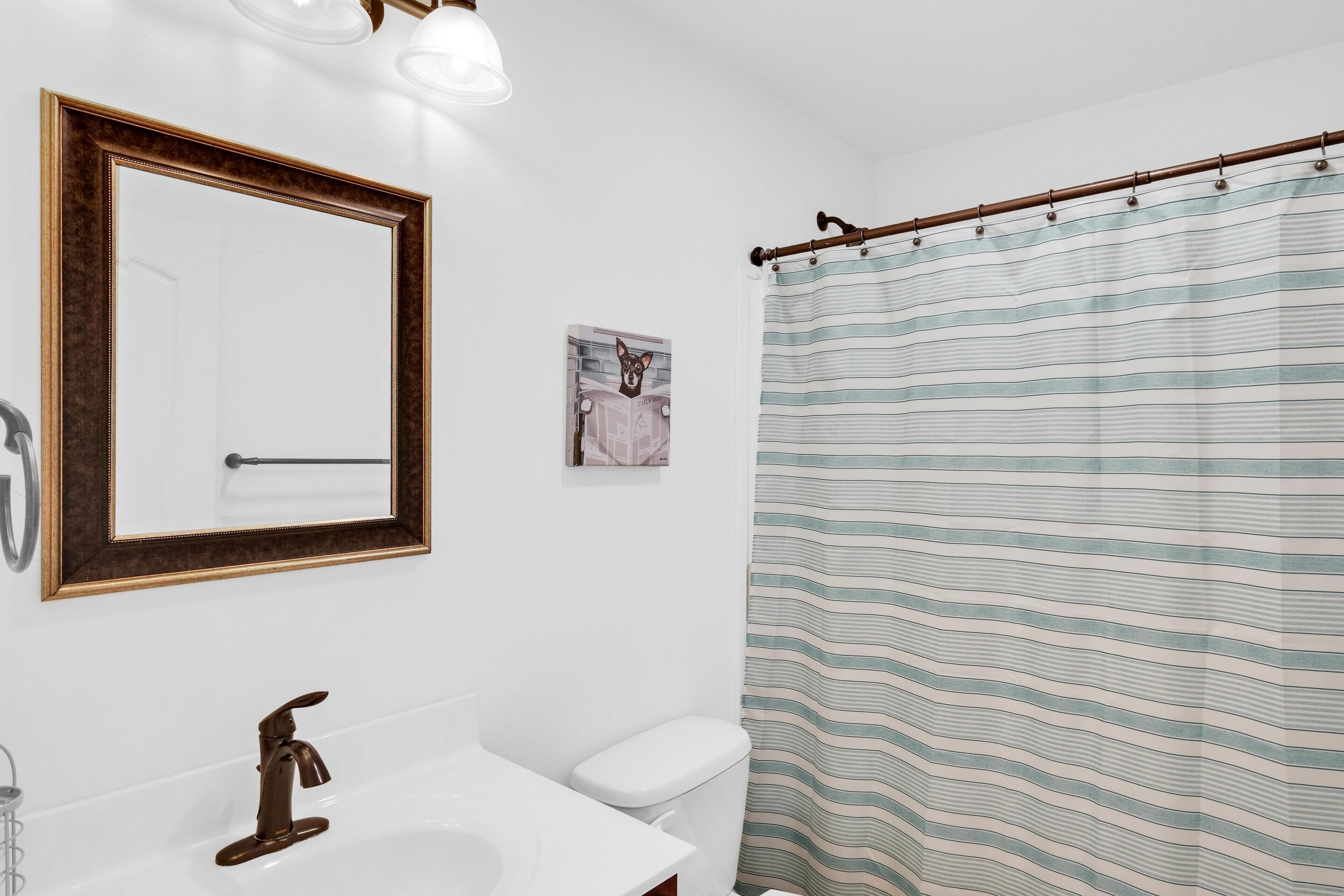 A bathroom with a white sink, a mirror with a wooden frame, a toilet, and a striped shower curtain.