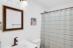 A bathroom with a white sink, a mirror with a wooden frame, a toilet, and a striped shower curtain.