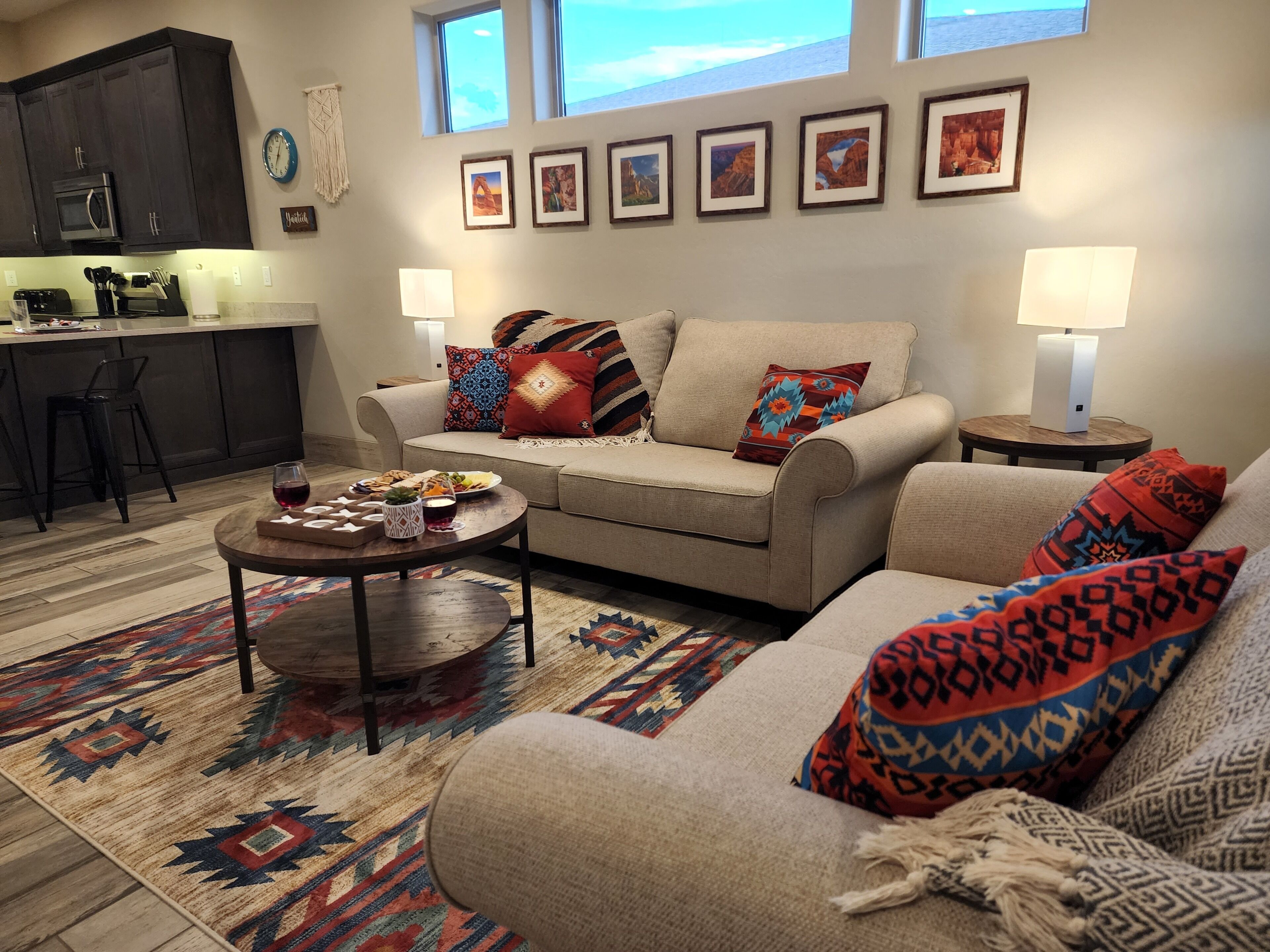 Ein Wohnzimmer mit einer Couch, einem Couchtisch und einem Teppich. Es gibt eine Küchenzeile mit einer Mikrowelle und einer Uhr.