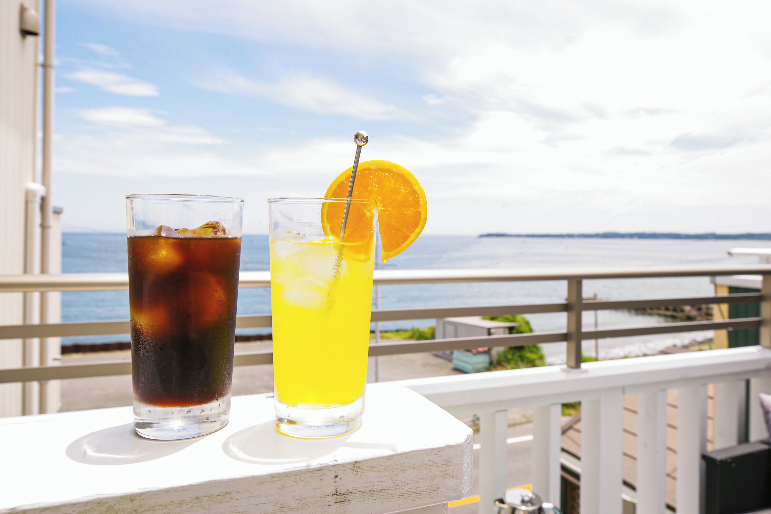 Two glasses of beverages on a balcony with a view of the sea.