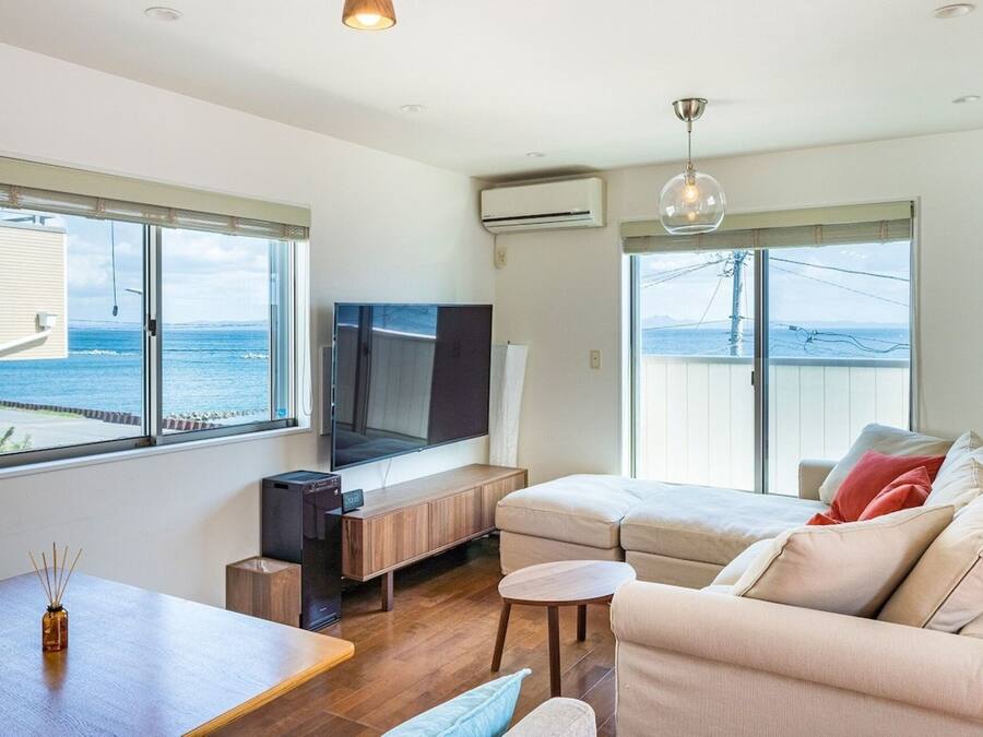 Una sala de estar moderna con un televisor de pantalla plana grande, asientos cómodos y ventanas amplias que ofrecen vistas al mar.