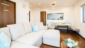 Ein modernes Wohnzimmer mit einer Eckcouch, einem Esstisch mit Stühlen, Holzboden und einem großen Fenster.