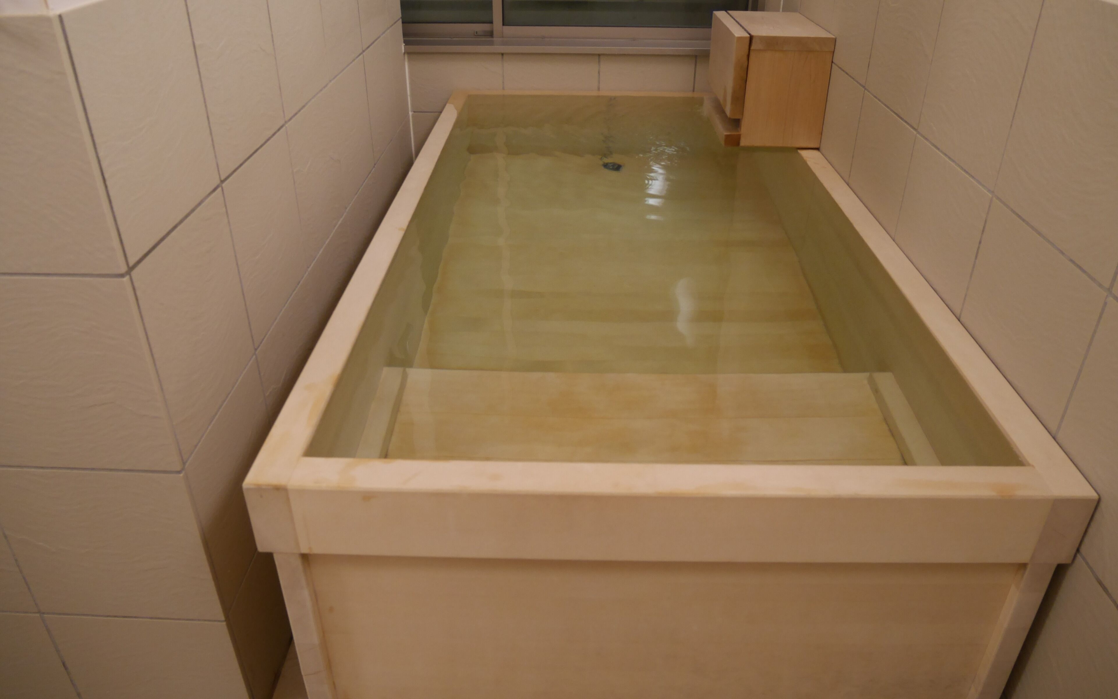 A rectangular bathtub with a glass front, surrounded by beige tiles.